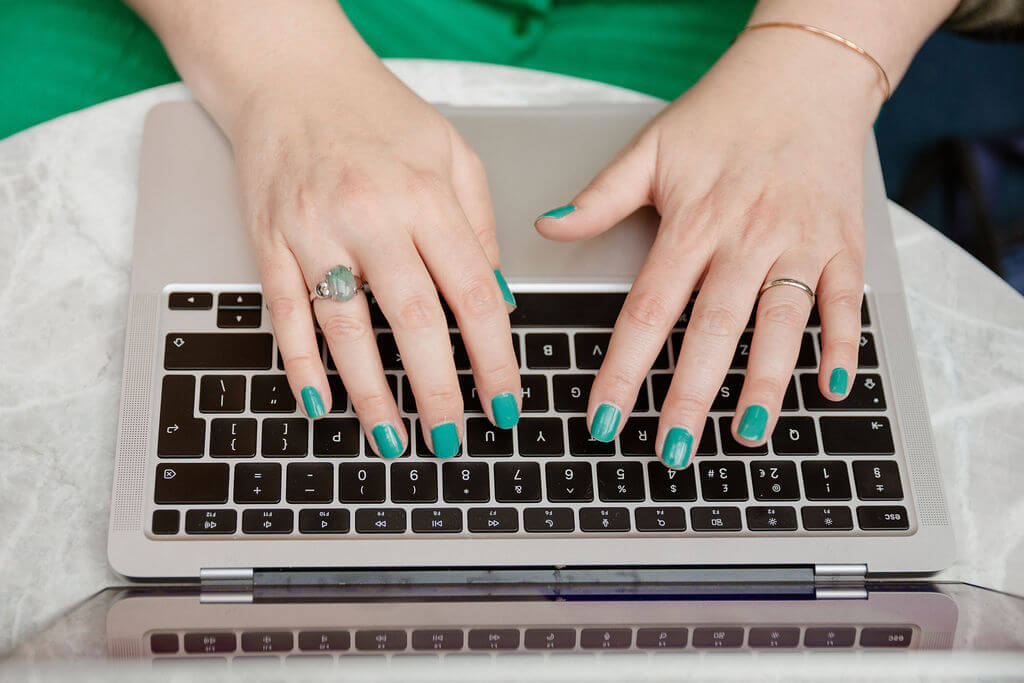 Jennifer's hands typing on her laptop. Her nails are painted green and she's wearing a green ring on her right ring-finger.
