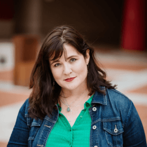 Headshot of Jennifer - she's a white woman with brown hair, who's wearing a green top and denim jacket.
